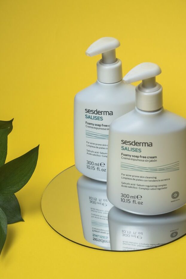 Close-up of skincare foamy soap-free cream bottles on a mirror with a yellow backdrop.