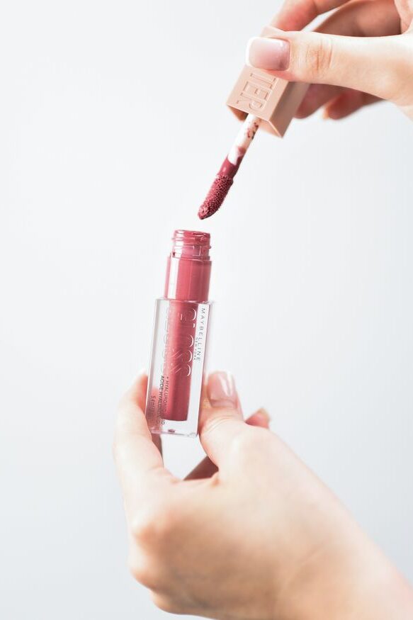 Close-up of hands using pink liquid lipstick. Ideal for beauty product shoots.