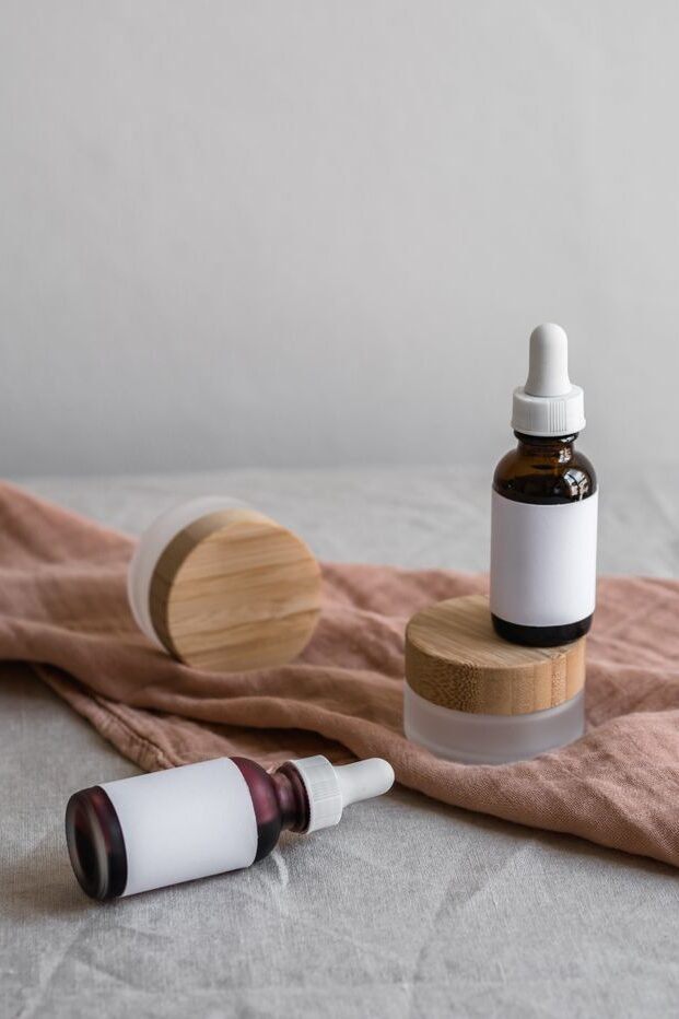 Elegant arrangement of cosmetic bottles with dropper lids on a soft textile surface.