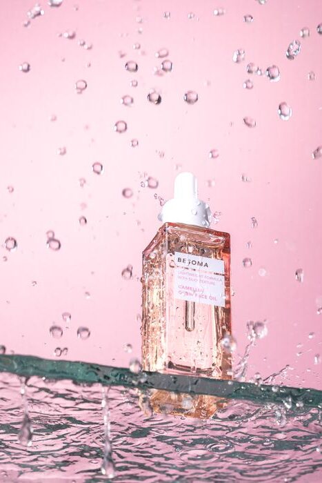 A studio shot of an elegant cosmetic serum with water splashes on a pink background.